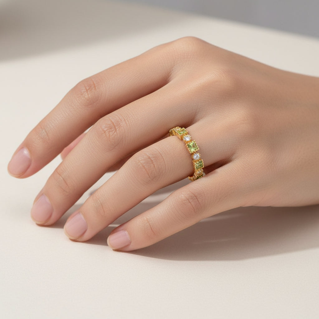 A close-up of a hand wearing a gold eternity ring set with alternating yellow and clear gemstones, resting on a light beige surface.